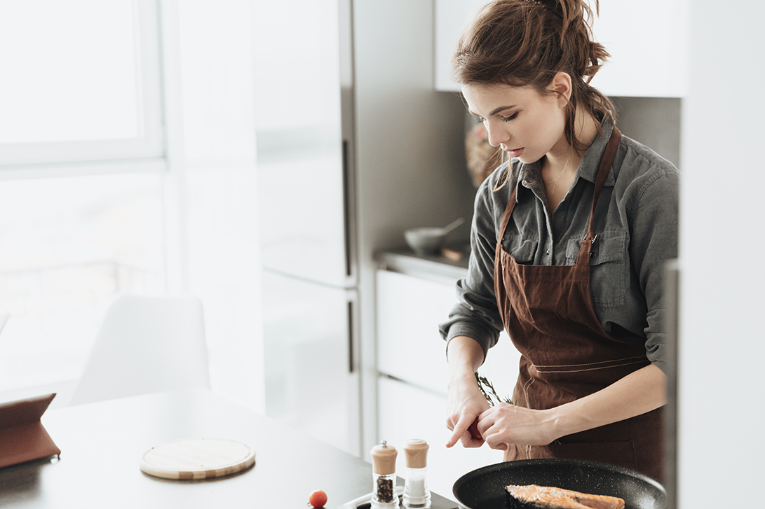 Pretty lady standing in kitchen while cooking fish
